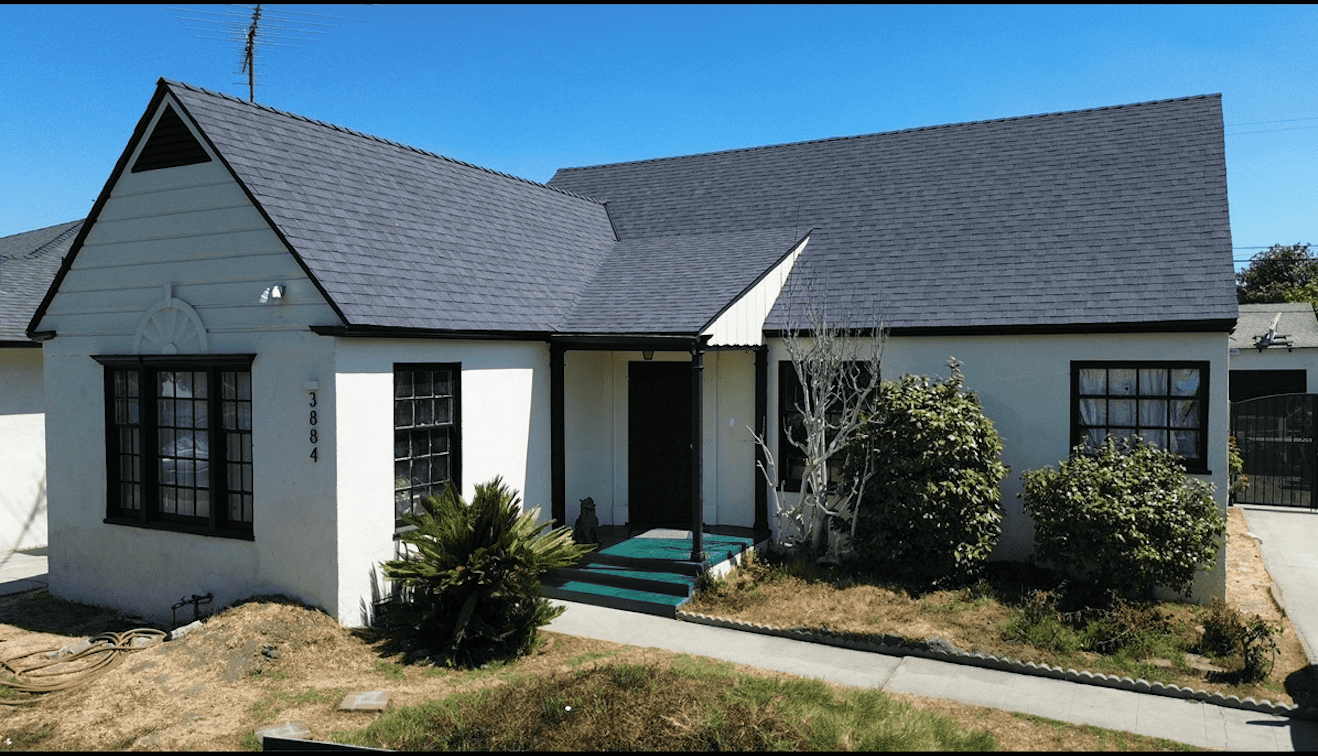 White cottage with black window frames and a dark gray roof under a clear blue sky.
