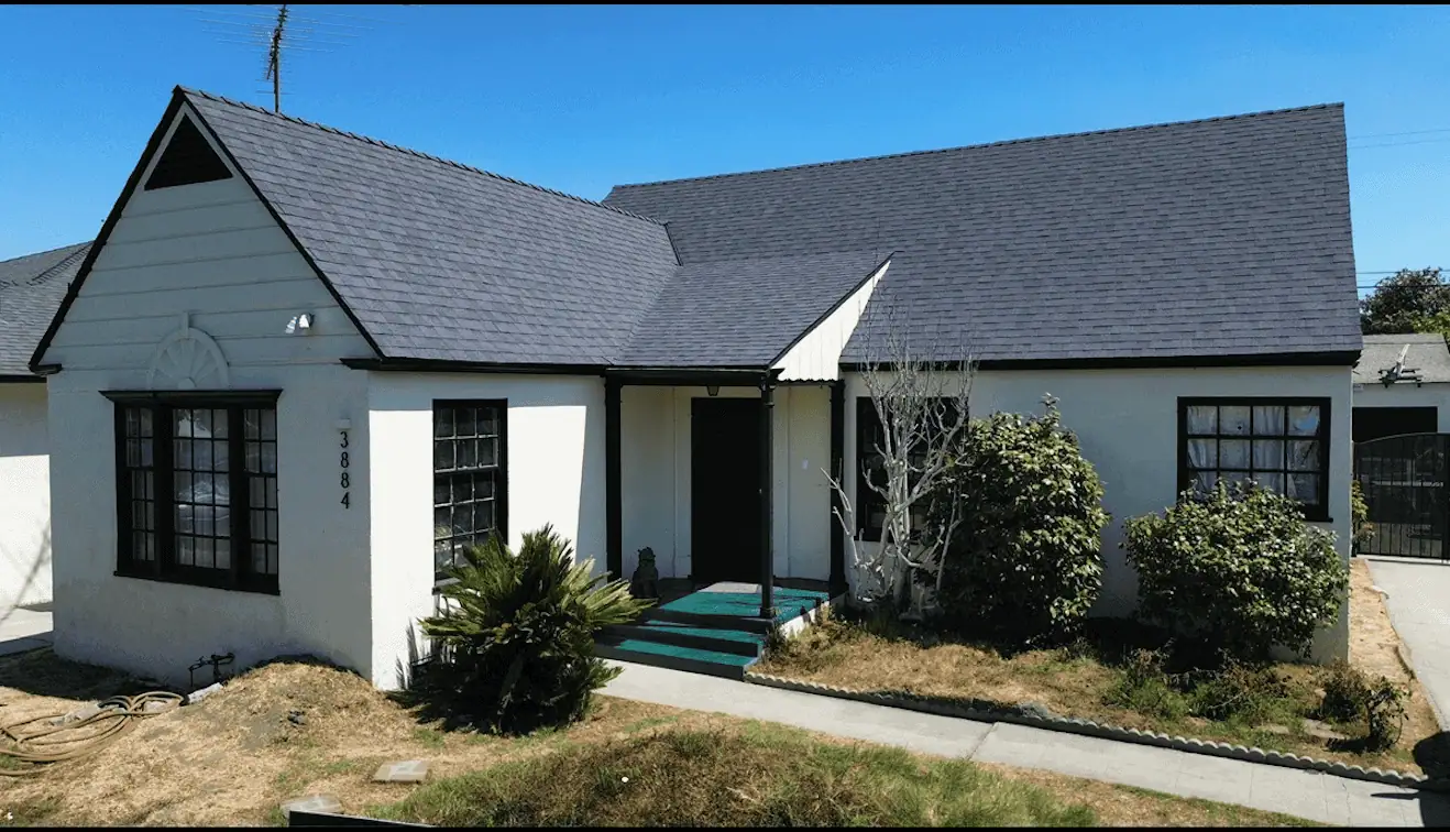 White cottage with black window frames and a dark gray roof under a clear blue sky.