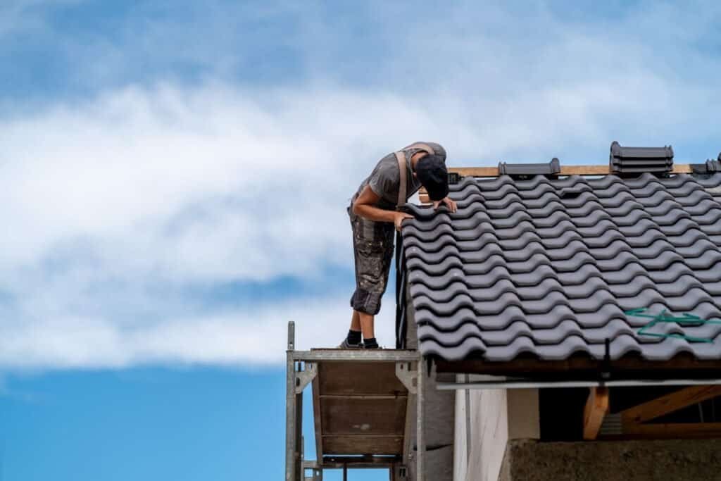 Roofing contractor installing roof tiles on residential home.