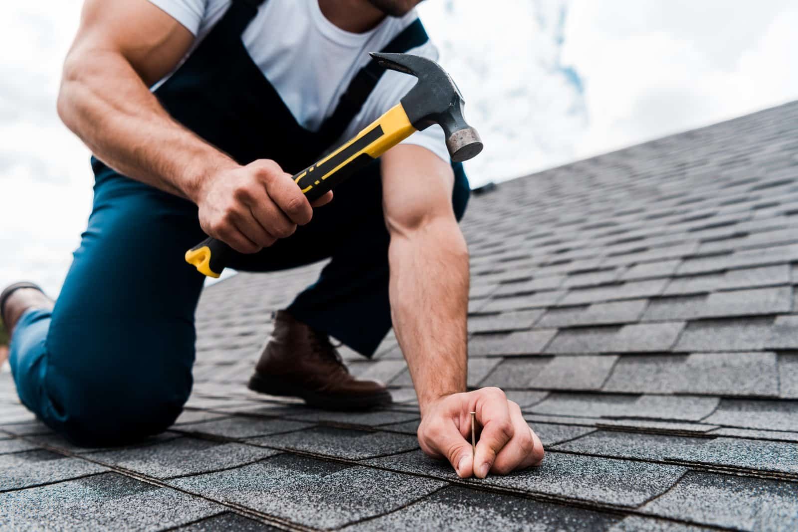 Man repairing roof shingles with hammer during roofing service.