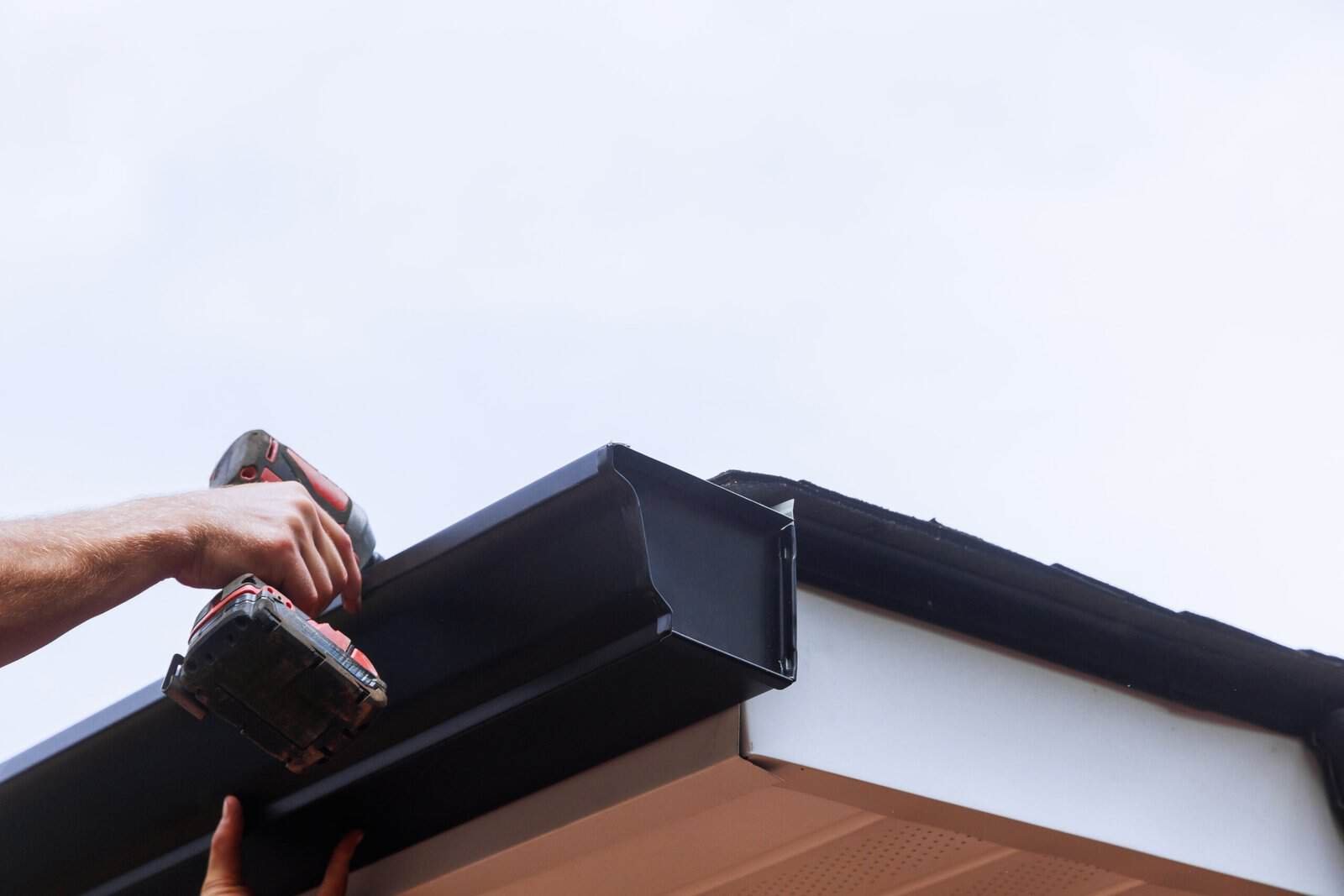 Professional installing a black gutter on a roof edge for roofing services.
