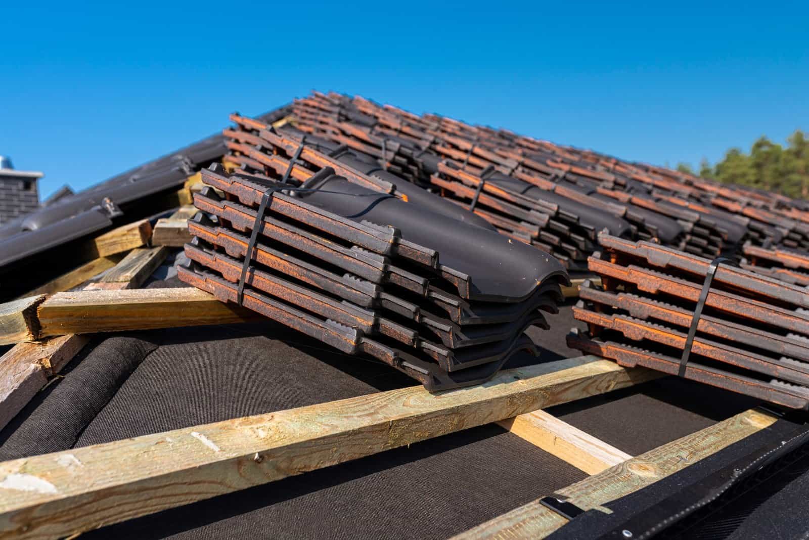 Roofing tiles being installed on a house roof with wooden support structure.